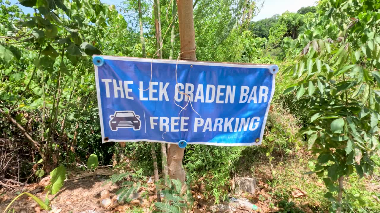 Blue restaurant parking sign moves gently in bright daylight, surrounded by lush tropical greenery