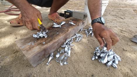 persona que utiliza pinzas para manejar metal fundido caliente vertido en moldes, en una tabla de madera, al aire libre, durante el día