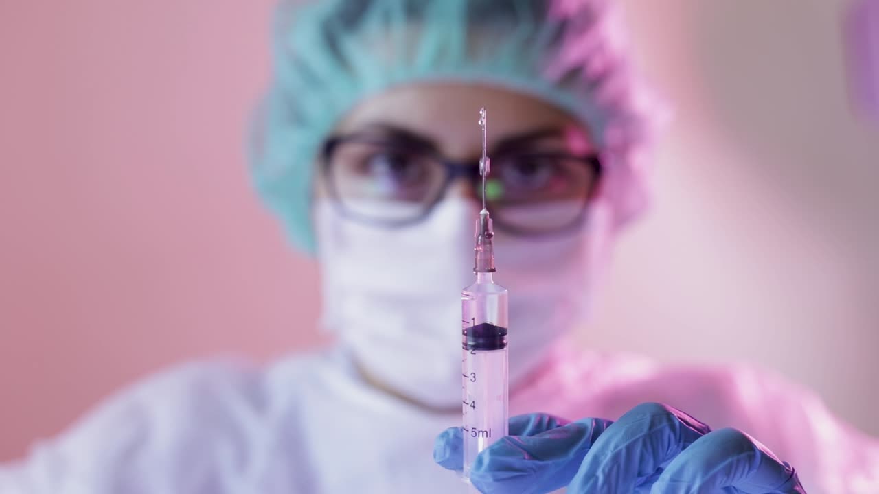 Close up focused injection needle holding by hands with gloves of unfocused nurse wearing mask for protection by Coronavirus