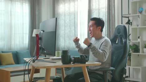 asian cameraman in long sleeved t-shirt and black pants being happy finishing editing photos by desktop computer while working at home.