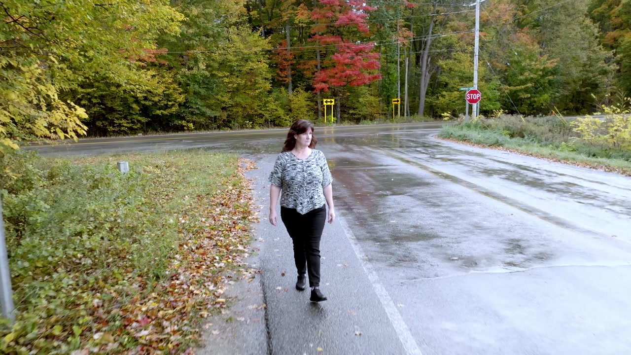 Middle aged caucasian woman walking along a road in Northern Michigan with fall colors and drone video pulling back.