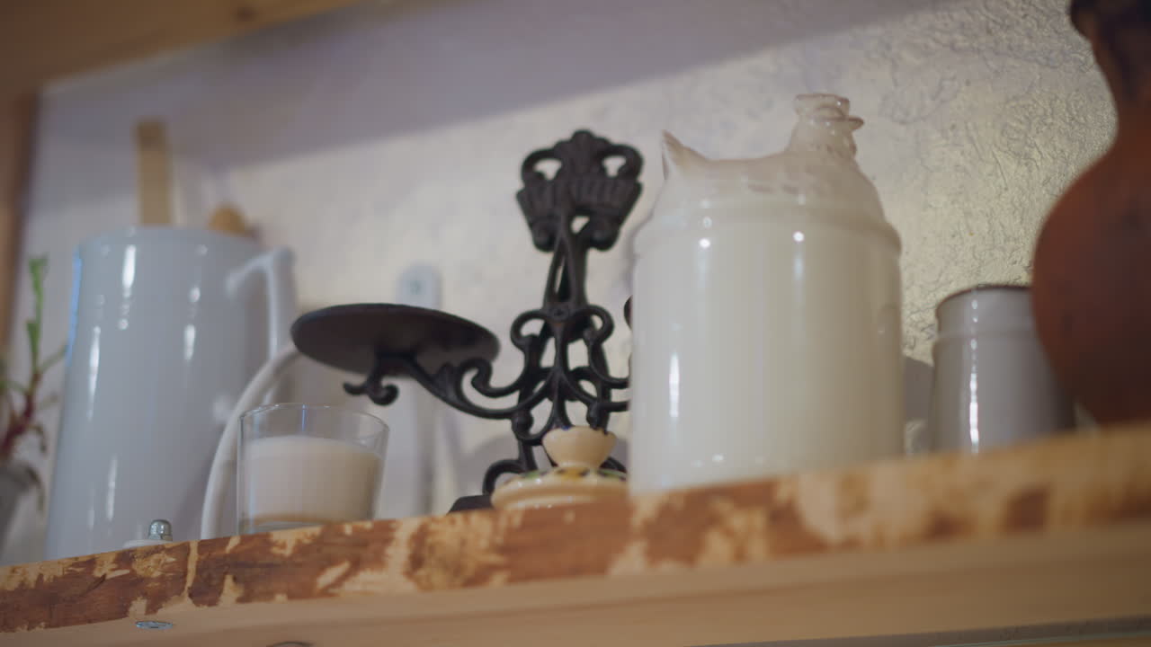 Barattoli di smalto bianco su uno scaffale di legno, sottopentola in ferro e vernice scheggiata, calda luce mattutina, cuoco casalingo che sistema gli utensili, natura morta nostalgica di una cucina rustica, texture di ceramica e metallo.