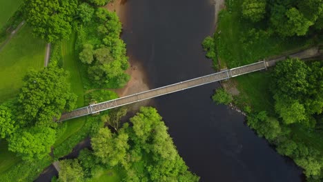 aerial drone footage of a bridge over water in a green park in summer