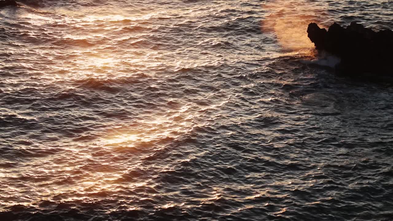 Onde al tramonto in slow motion che riflettono la luce dorata sulla superficie del Mar Mediterraneo a Ibiza.