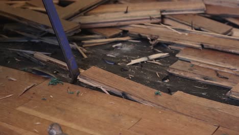 primer plano de un trabajador de cuello azul usando una barra de palanca para quitar el suelo de madera dañado por el agua