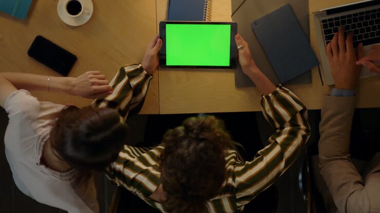 Woman showing project to colleagues on green screen device. Team using tablet.