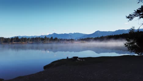 Lake-with-mist-approached-from-shore-with-fire-pit-tilt-Enid-British-Columbia-Canada