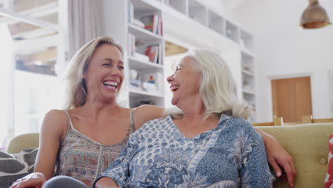 mother with adult daughter watching movie on sofa at home together