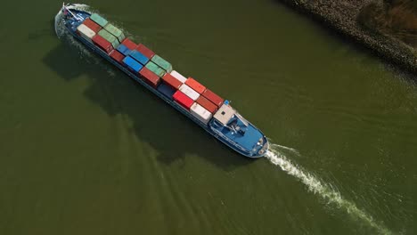 Top-down-aerial-view-of-a-huge-container-ship-navigating-through-the-canals-of-Zwijndrecht,-The-Netherlands