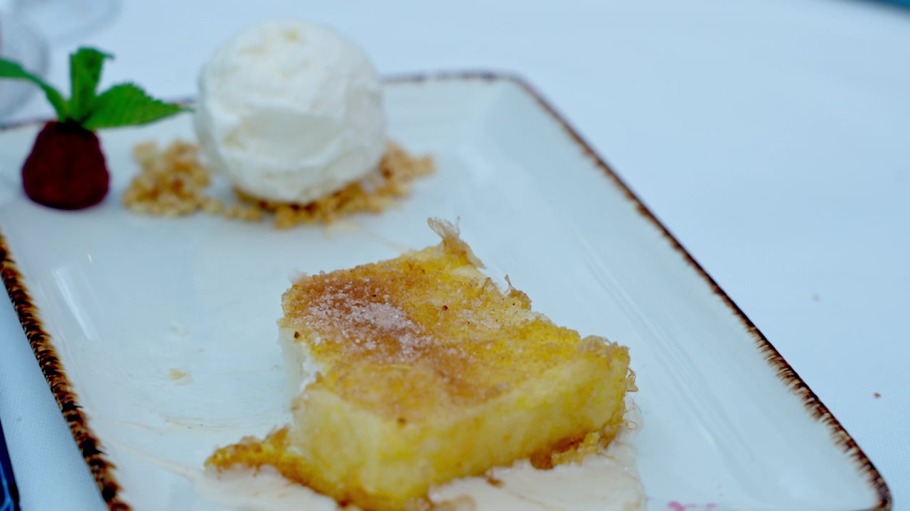 Sweet pastry, possibly fried or baked, topped with sugar crystals, served on a white plate with vanilla ice cream and a raspberry