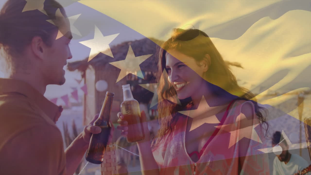 On beach, couple clinking beer bottles, animation of flag overlaying scene