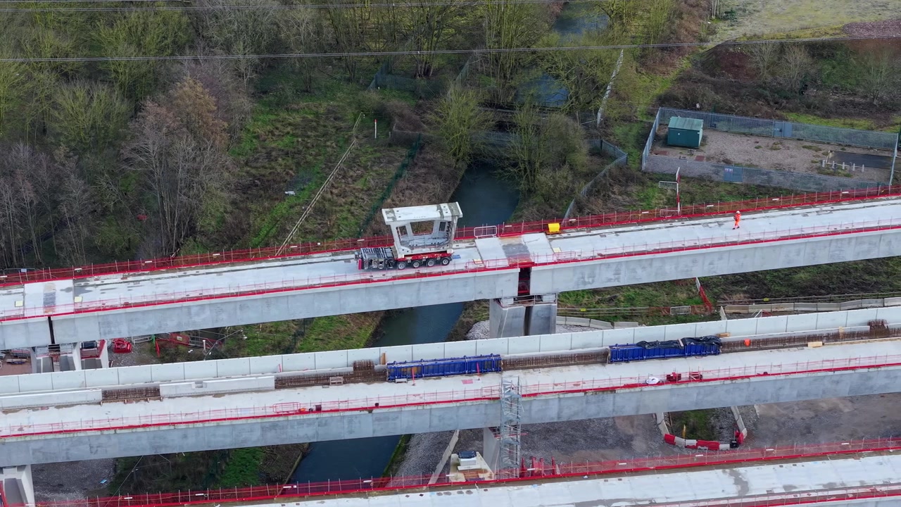 Vista de drone da infraestrutura de construção ferroviária de alta velocidade mostrando um transportador de carga pesada movendo uma grande seção de viga de concreto no local em Coleshill, Reino Unido
