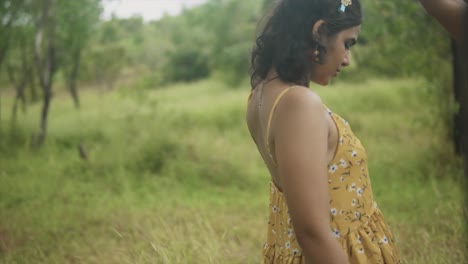 A-slow-motion-shot-of-a-beautiful-young-Asian-female-wearing-a-floral-dress-twirling-as-she-dances-carefree-in-a-grass-field-outdoors,-India