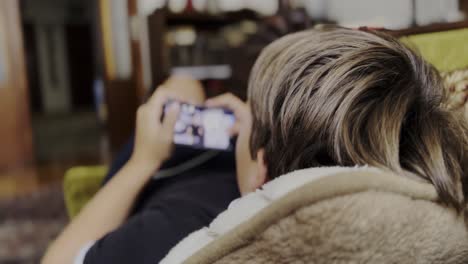 young boy relaxing on sofa, focused on scrolling smart phone screen