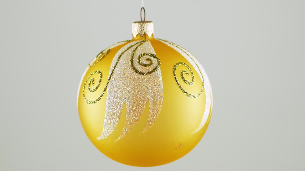 Golden Christmas ball toy turning round and back in luminous light on dark green background. New Year pattern.