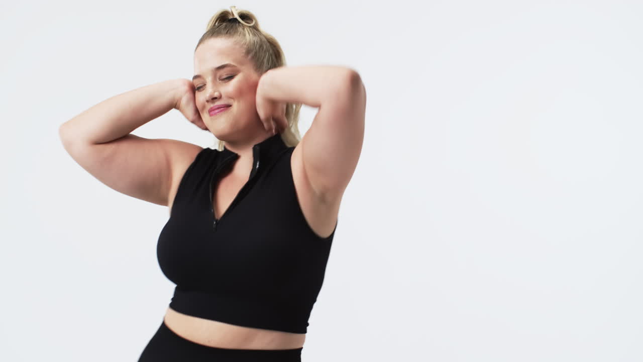 Donna caucasica curvy con capelli biondi a coda di cavallo che balla in studio, con spazio per il testo.