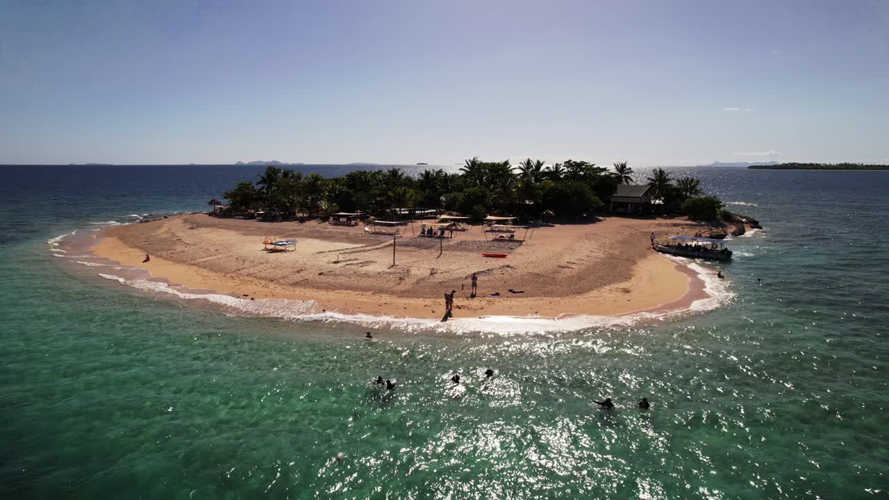 drone estático con vistas a una pequeña isla tropical en fiji mientras la gente nada en el agua en un día azul claro
