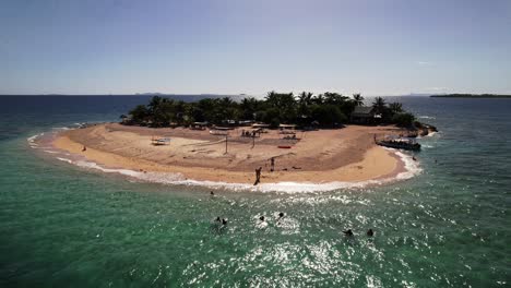 Static-Drone-overlooking-a-small-tropical-island-in-Fiji-while-people-swim-in-the-water-on-a-clear-blue-day