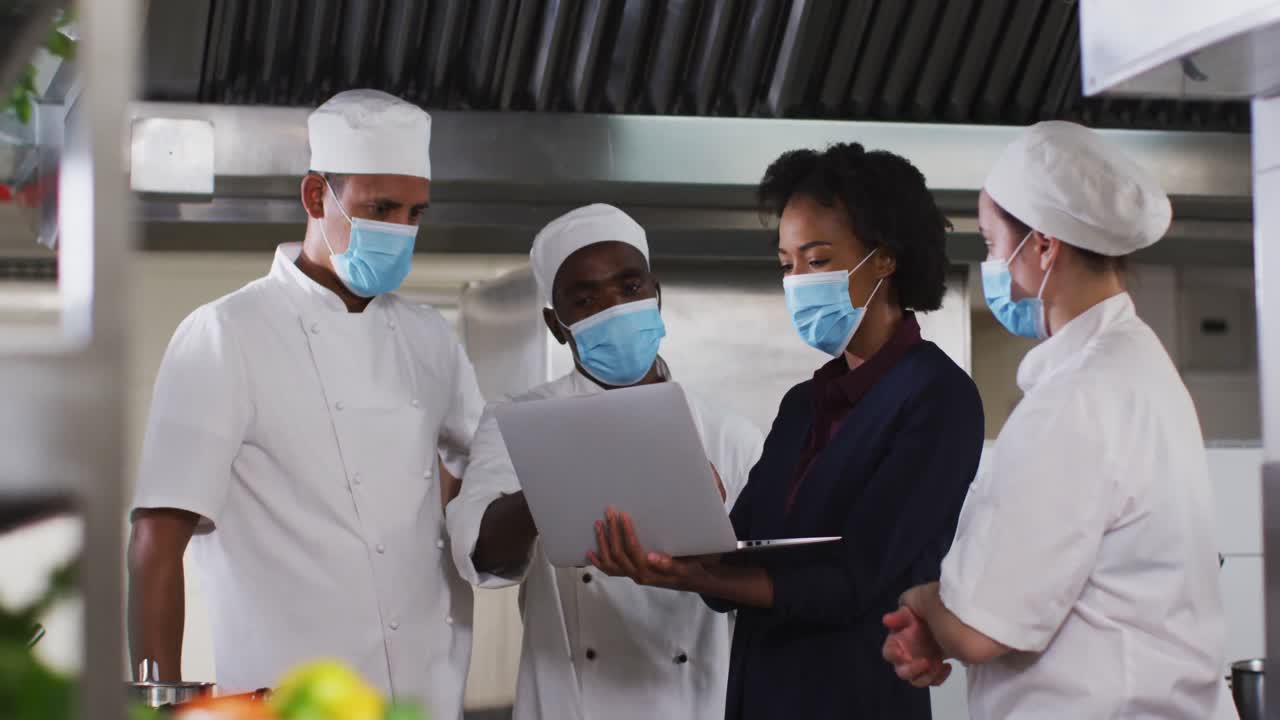African american female manager talking with chefs wearing face masks in restaurant kitchen