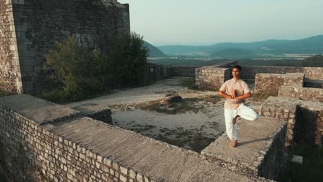 Orbit-Zeitlupenaufnahme-Eines-Asiatischen-Indischen-Mannes,-Der-Yoga-Pose-Macht-Und-Bei-Sonnenaufgang-Das-Schloss-Hinter-Sich-Genießt