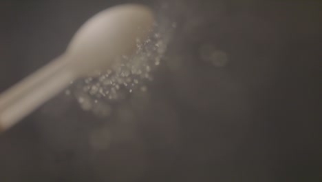 sugar falling down on camera lens from wooden spoon in slow motion