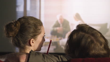 rear view of couple hugging sitting in the cinema while they watching a movie and talking