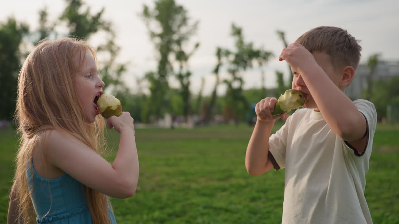 children holding pears together in cheers gesture during picnic in park, smiling and sharing playful moment in green summer setting, healthy snack bonding