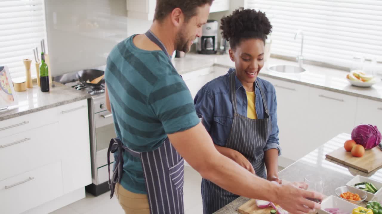 Video de pareja feliz y diversa preparando una comida, cortando verduras en la cocina