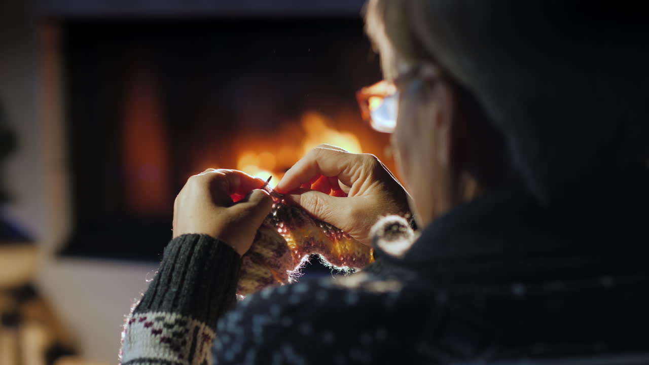 할머니는 벽난로 옆에서 따뜻한 스카프를 짠다 4k 비디오