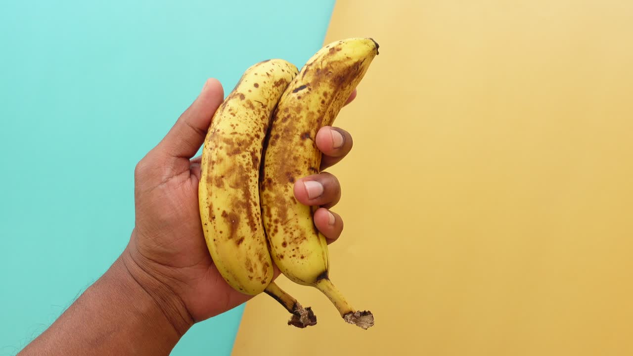 갈색 반점이 있는 두 개의 익은 바나나를 들고 있는 사람