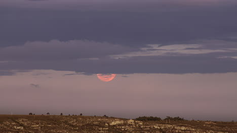 rise of full glowing red moon with clouds above the horizon of the earth