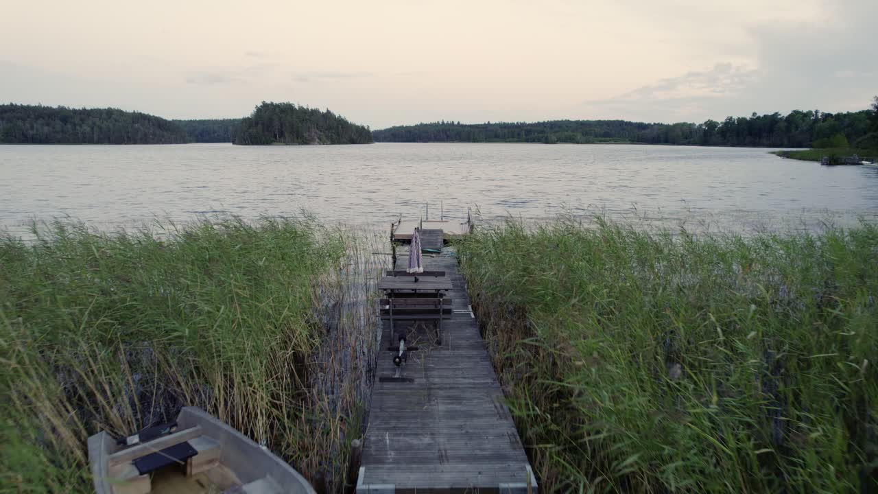 drone pov disparado a lo largo de un pequeño muelle de madera cubierto al atardecer, suecia