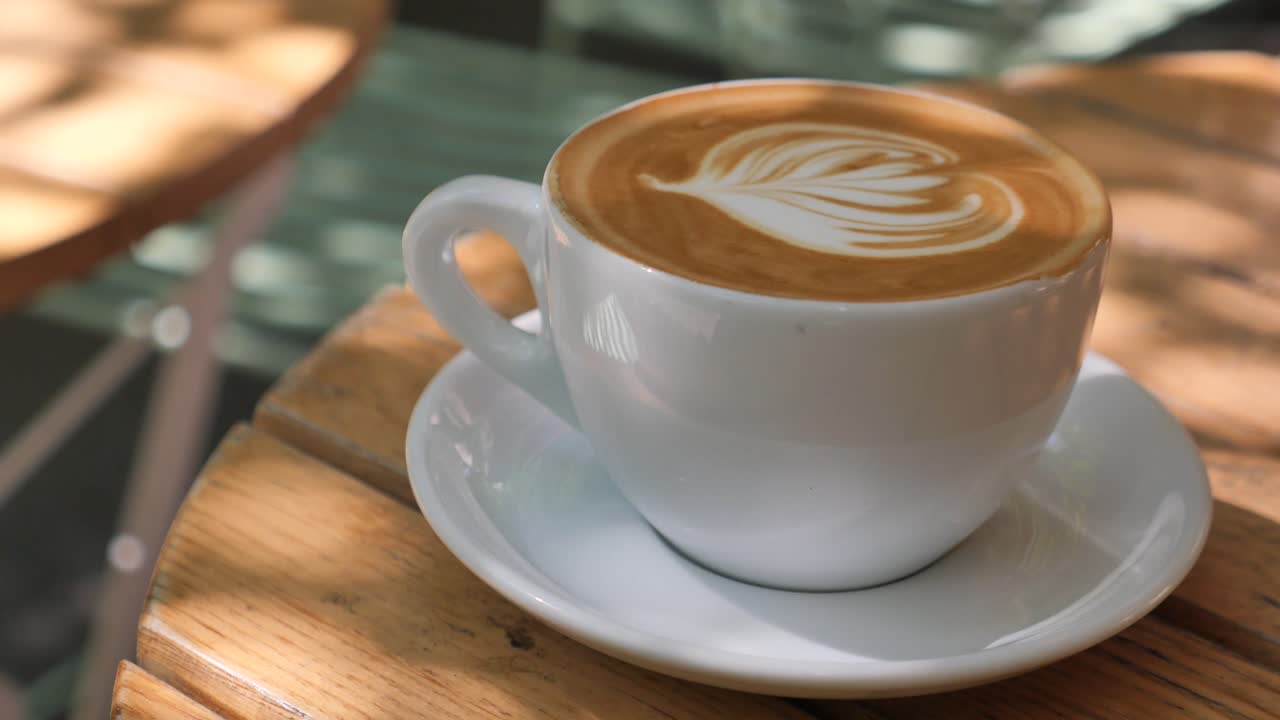 A cup of latte with art on a wooden table in sunlight