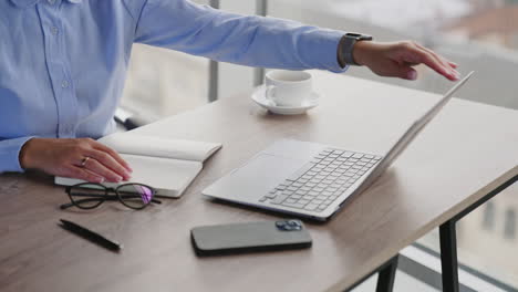 unrecognizable woman sitting at desk. female hands close laptop and paper notebook. office employee finishes working day.