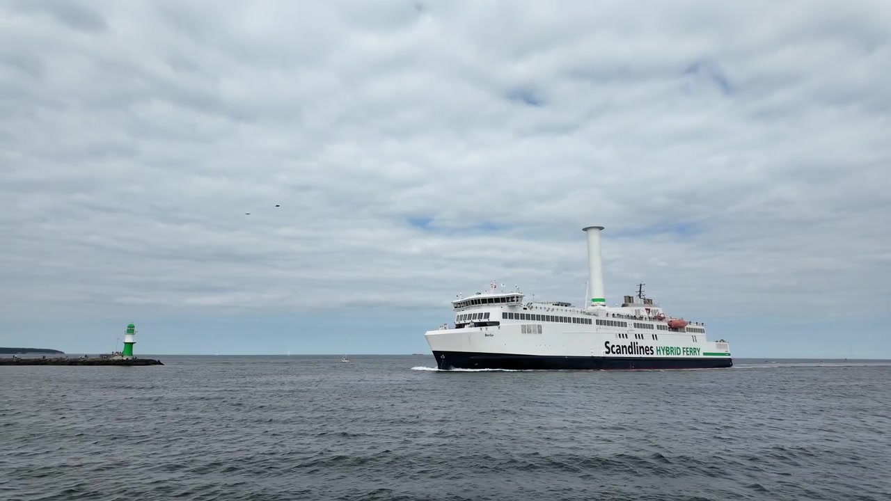 Scandlines hybridfærge Berlin passerer Warnemünde fyrtårn på Østersøen, hvilket fremhæver bæredygtig passagertransport, moderne maritim teknologi og kystrejser i Nordtyskland.
