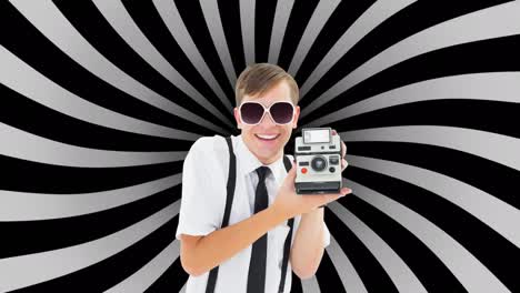 retrato de un hombre caucásico sosteniendo una cámara polaroid contra un fondo radial negro y gris