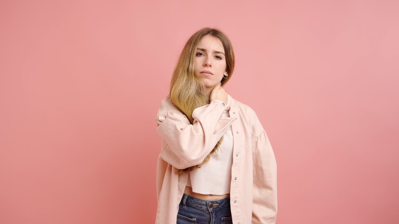Young woman massaging neck on pink background