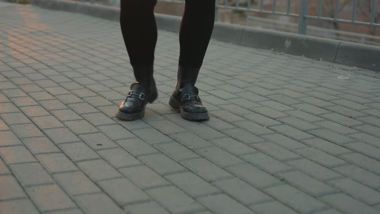 Alacakaranlıkta parke yürüyüş yolunda ayakların yakın çekim dansı, siyah botlarla odaklanmış ayak hareketleri ve ritmik adımlar, dokulu parke taşları, dinamik tempo ve şehir sokağı pratiğiyle azim ve hassasiyetin aktarılması.