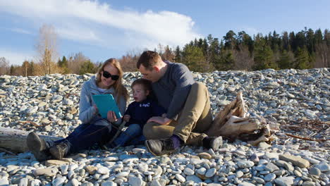 family of three sitting on the stony shore and watching something pad