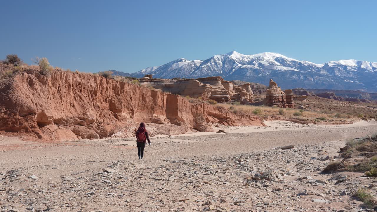 Solitary Woman With Backpack Walking in Desert Landscape With SNow Capped Mountains in Background