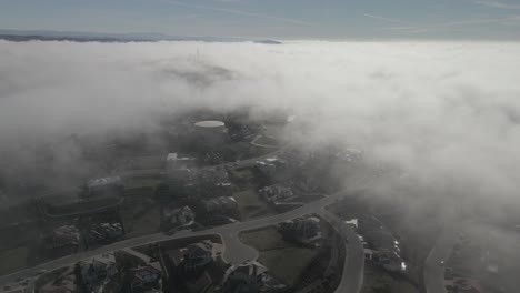 filmagem de drone através da linha de nuvens em uma manhã enevoada, mostrando folsom, eua em intervalos entre as nuvens, revelando um bairro abaixo