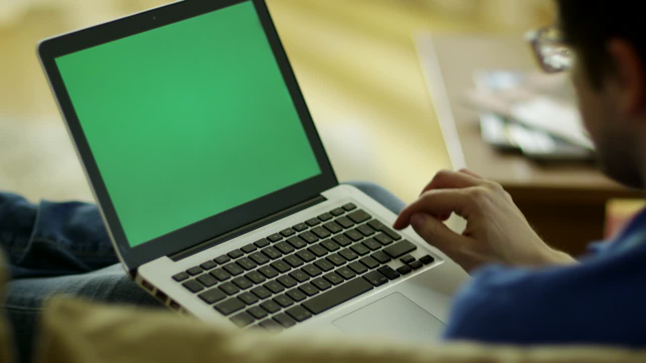 Man Laying on Couch and Using Laptop with Green Screen at Home