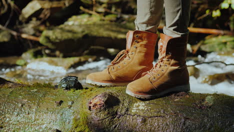 the feet of the traveler stand on a wet log near a mountain stream tourism and hiking conceptt