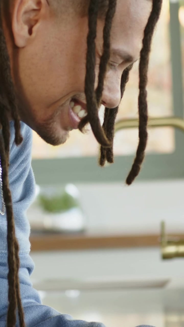 Uomo di mezza età sorridente, chinato in avanti, che si sistema i braccialetti e osserva un oggetto sul bancone della cucina.