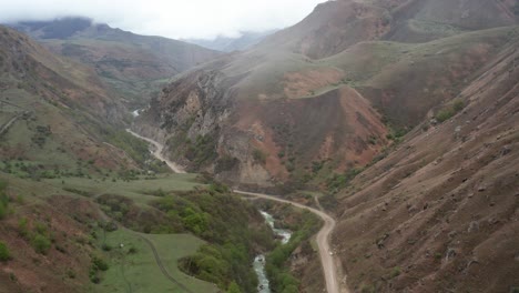 aerial shot of hilly landscape with winding river and road on cloudy day