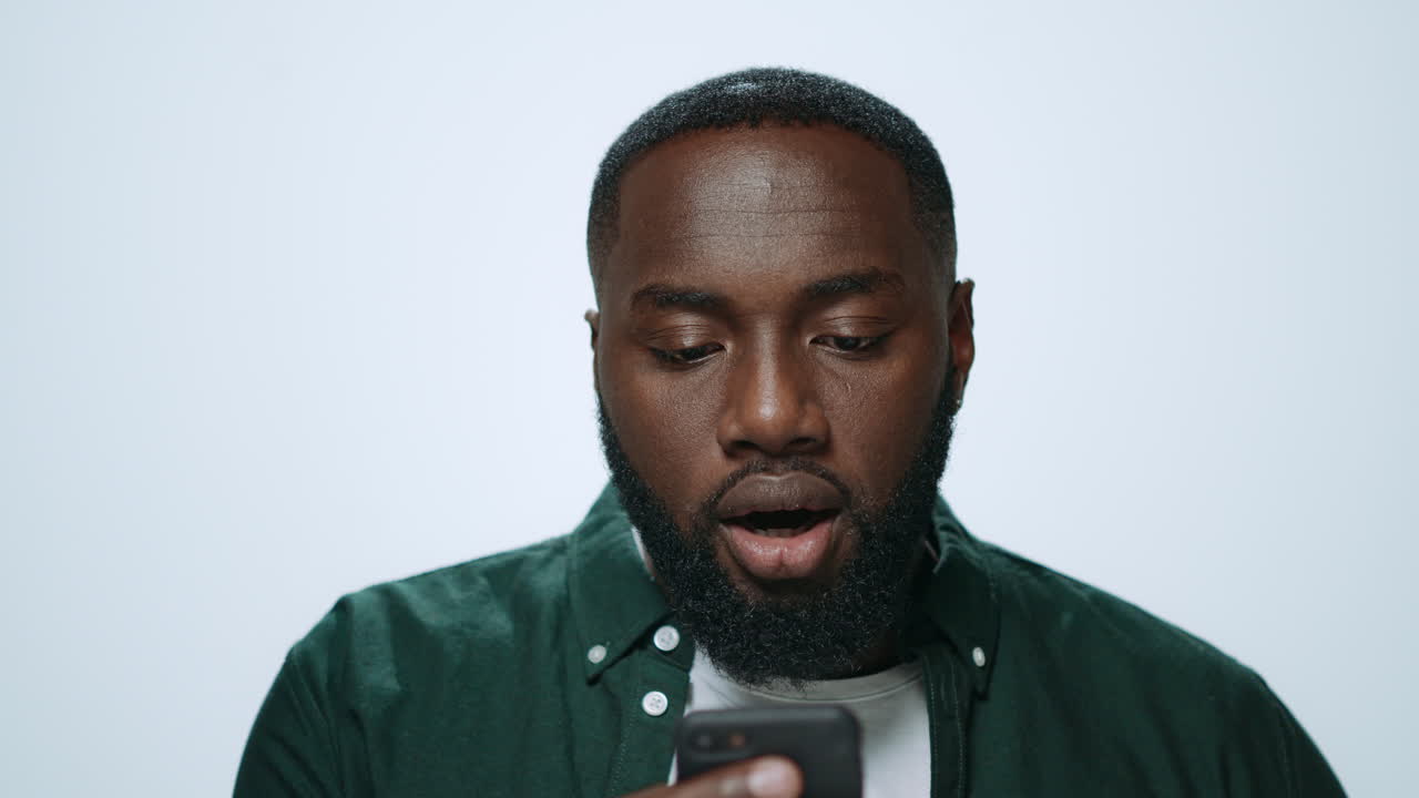 Portrait of emotional african man looking smartphone screen in grey background.