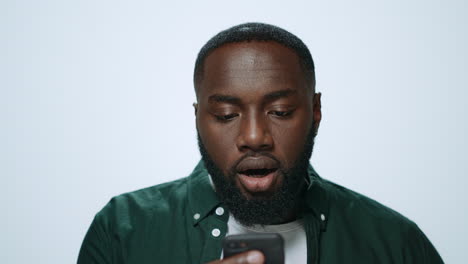 Portrait-of-emotional-african-man-looking-smartphone-screen-in-grey-background.