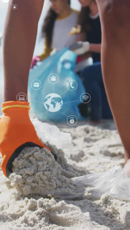 animation of globe icons over hand of biracial female volunteer picking up rubbish on beach