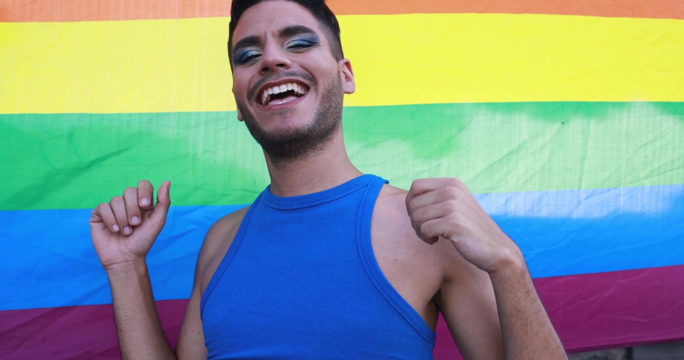 Homem feliz com maquiagem sorrindo em frente à bandeira arco-íris