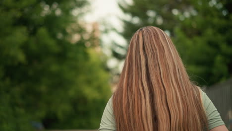 back view of young woman walking along a path with long, flowing blonde hair cascading down her back, surrounded by lush greenery, she walks thoughtfully